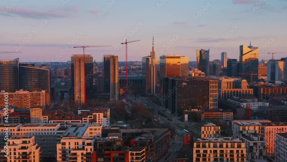Drone aerial view flying over towards downtown city center featuring sunset cityscape panorama with cranes construction sites and a canal with an orange red yellow blue sky and clouds Drone aerial view flying over towards downtown city center featuring sunset cityscape panorama with cranes construction sites and a canal with an orange red yellow blue sky and clouds