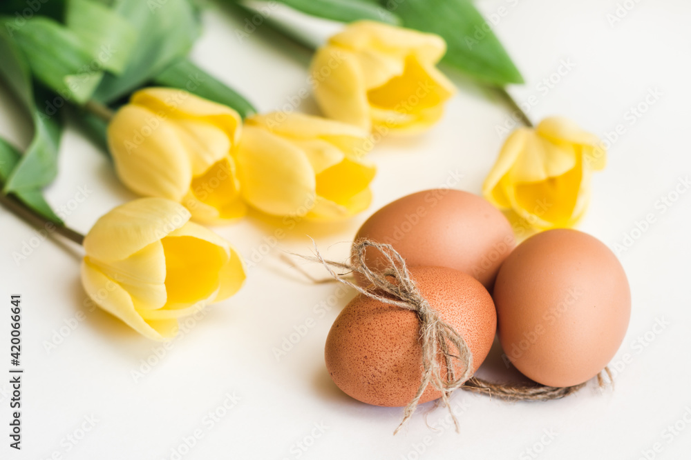Three brown chicken eggs and yellow tulips on a white background Three brown chicken eggs and yellow tulips on a white background