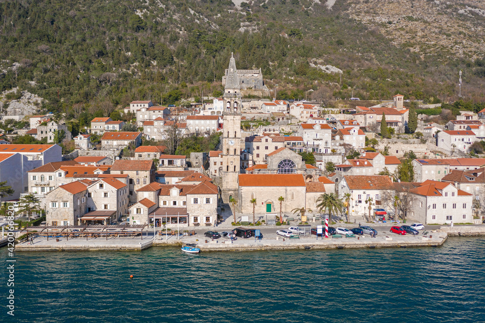 Aerial shot of the old coastal town of Perast at the foot of the mountain. Seaside promenade, residential buildings with traditional balkan red roofs, ancient Cathedral and coastline