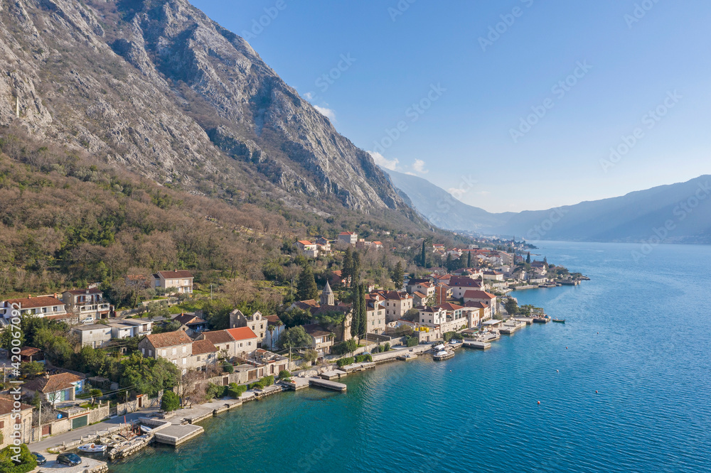 Aerial shot of the old coastal town of Perast at the foot of the mountain. Seaside promenade, residential buildings with traditional balkan red roofs, ancient Cathedral and coastline