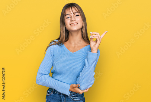 Teenager caucasian girl wearing casual clothes with a big smile on face  pointing with hand and finger to the side looking at the camera.