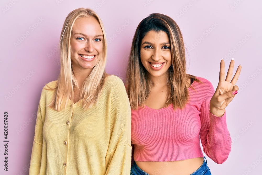 Two friends standing together over pink background showing and pointing up with fingers number three while smiling confident and happy. Two friends standing together over pink background showing and pointing up with fingers number three while smiling confident and happy.
