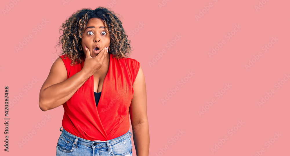 Young african american plus size woman wearing casual style with sleeveless shirt looking fascinated with disbelief, surprise and amazed expression with hands on chin Young african american plus size woman wearing casual style with sleeveless shirt looking fascinated with disbelief, surprise and amazed expression with hands on chin