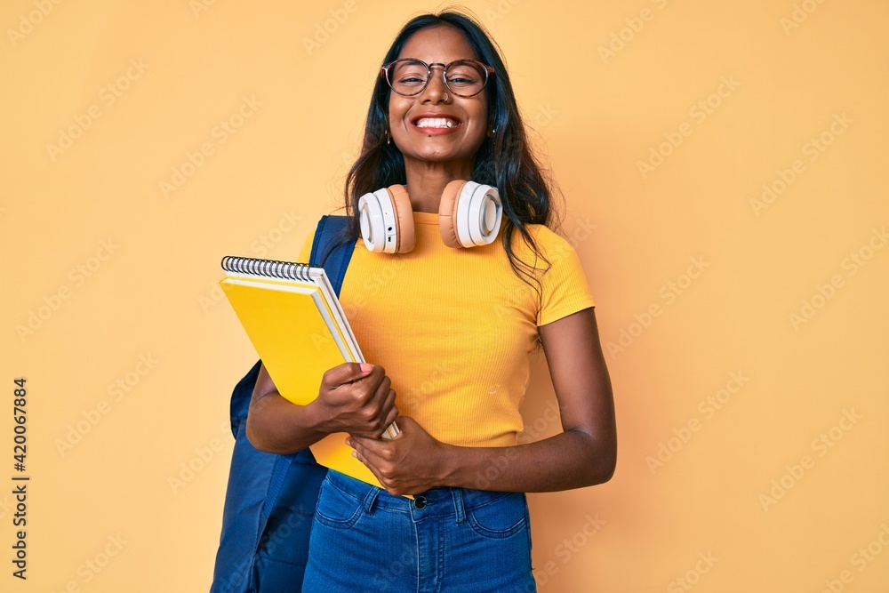 Young indian girl holding student backpack and books looking positive and happy standing and smiling with a confident smile showing teeth Young indian girl holding student backpack and books looking positive and happy standing and smiling with a confident smile showing teeth