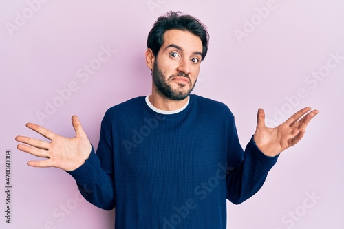 Young hispanic man wearing casual clothes clueless and confused with open arms, no idea and doubtful face.