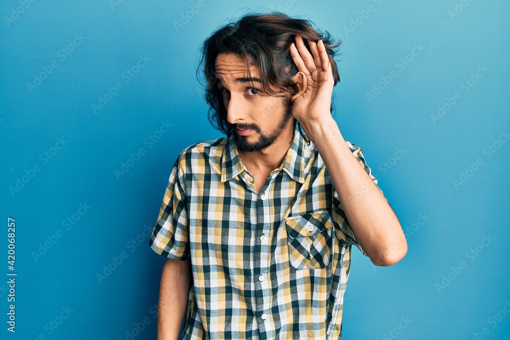 Young hispanic man wearing casual clothes smiling with hand over ear listening an hearing to rumor or gossip. deafness concept. Young hispanic man wearing casual clothes smiling with hand over ear listening an hearing to rumor or gossip. deafness concept.