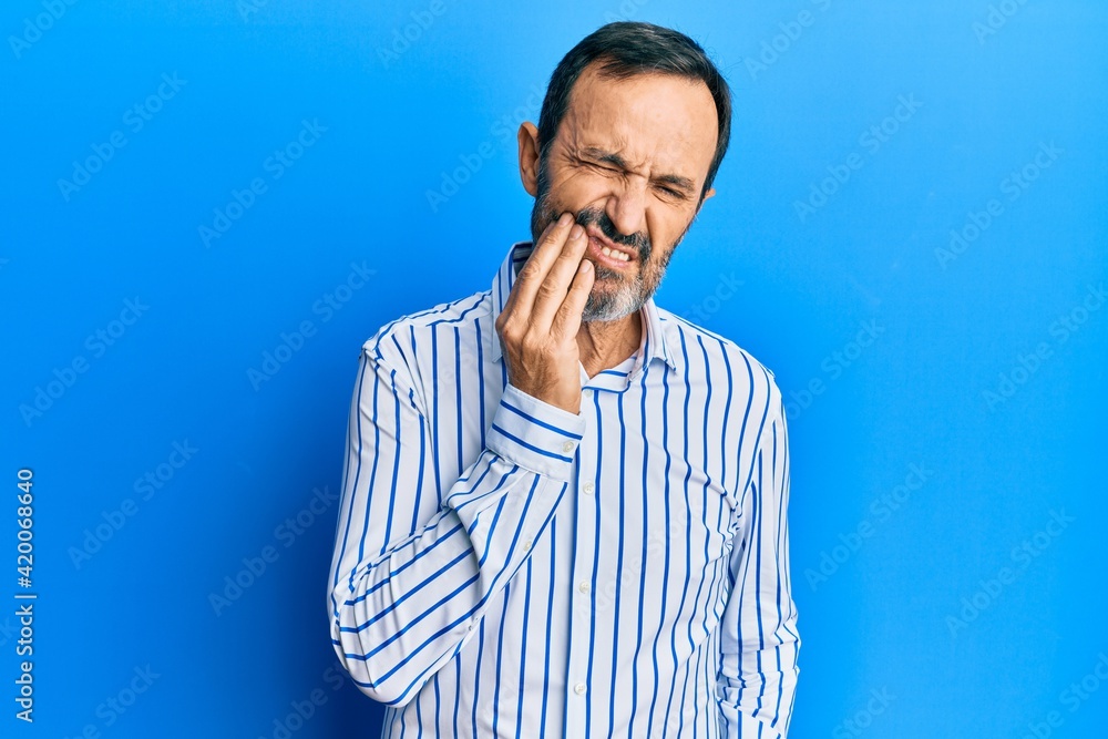 Middle age hispanic man wearing casual clothes touching mouth with hand with painful expression because of toothache or dental illness on teeth. dentist Middle age hispanic man wearing casual clothes touching mouth with hand with painful expression because of toothache or dental illness on teeth. dentist