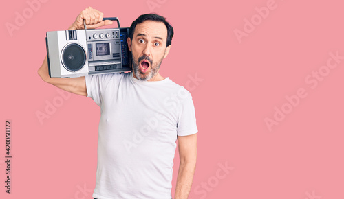 Middle age handsome man listening to music using vintage boombox scared and amazed with open mouth for surprise, disbelief face