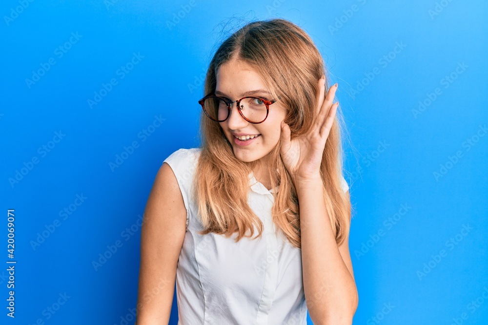 Beautiful young caucasian girl wearing casual clothes and glasses smiling with hand over ear listening and hearing to rumor or gossip. deafness concept. Beautiful young caucasian girl wearing casual clothes and glasses smiling with hand over ear listening and hearing to rumor or gossip. deafness concept.