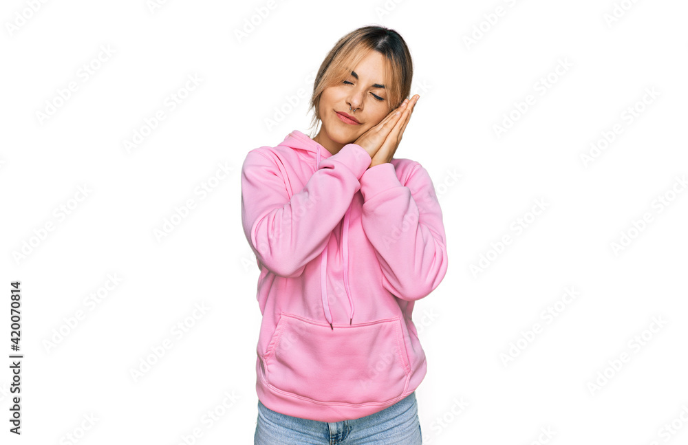 Young caucasian woman wearing casual sweatshirt sleeping tired dreaming and posing with hands together while smiling with closed eyes. Young caucasian woman wearing casual sweatshirt sleeping tired dreaming and posing with hands together while smiling with closed eyes.