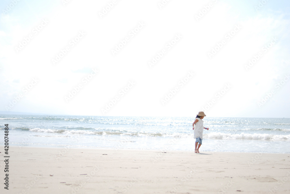 波と遊ぶ麦わら帽子をかぶった女の子、夏の海と砂浜の風景、コピースペースのある写真