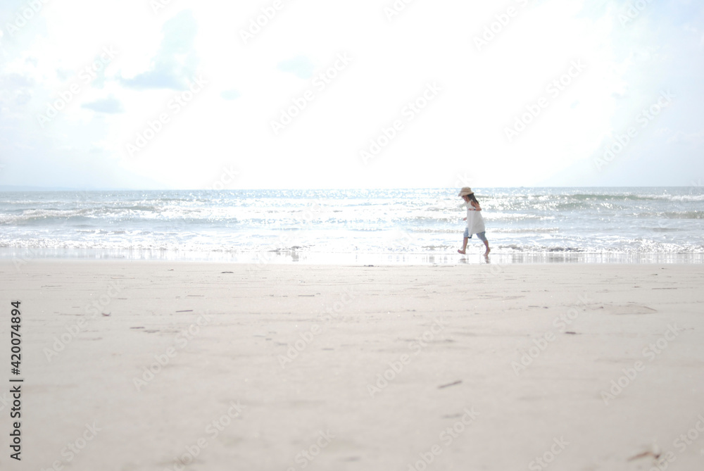 波と遊ぶ麦わら帽子をかぶった女の子、夏の海と砂浜の風景、コピースペースのある写真