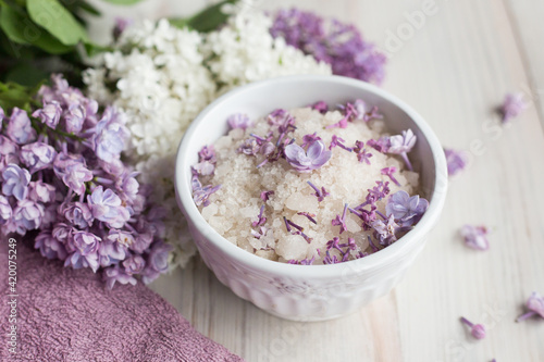 Homemade bath salt with fresh spring lilac flowers, home healthy spa, relaxation, light wooden background, purple towel, 