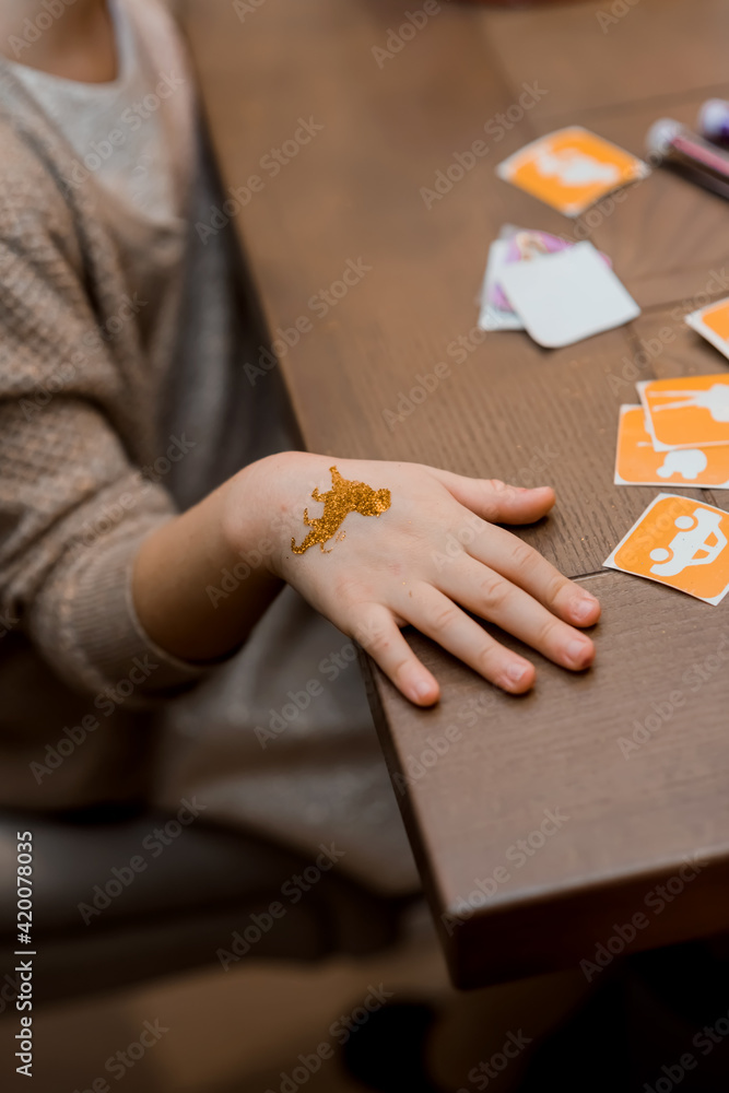 Obraz premium Close-up little child arm girl with tattoo sticker on body skin painted on it. Kid at a party event. Close up process of applying temporary tattoo on boy arm. Summer fun and child activities concept.