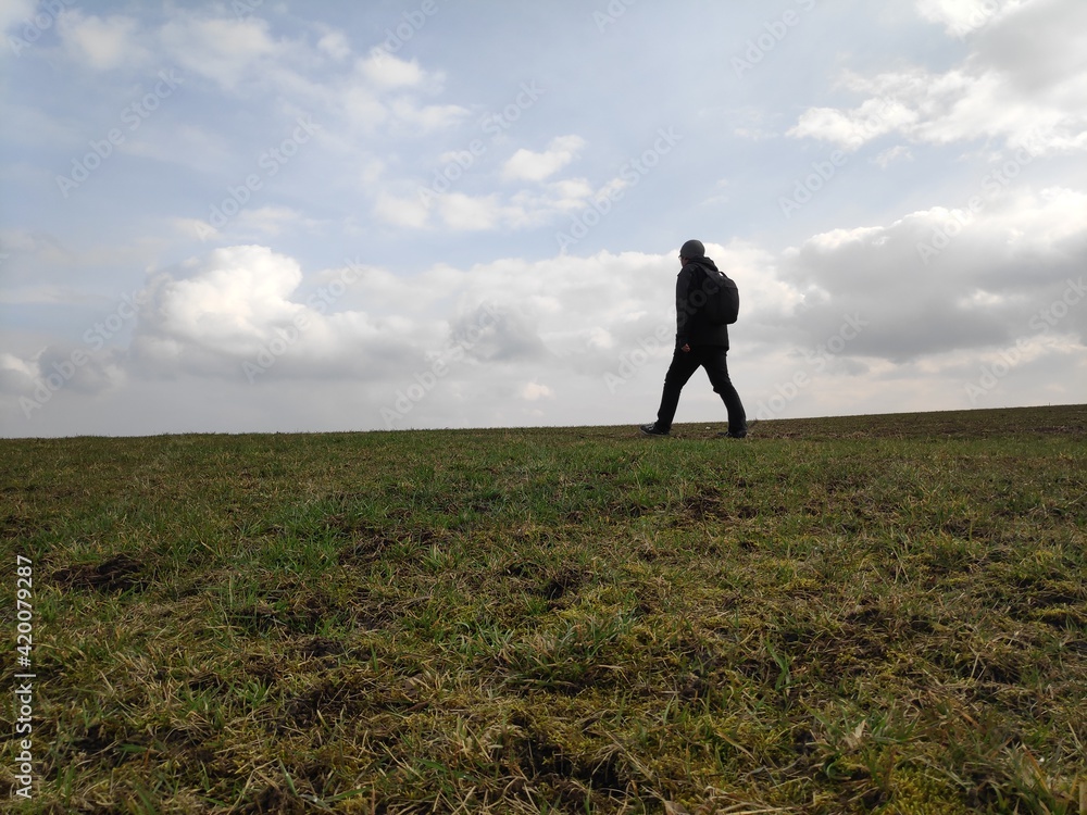 A man walking across a field on a day of dramtic clouds in rural Franconia in northern Bavaria.