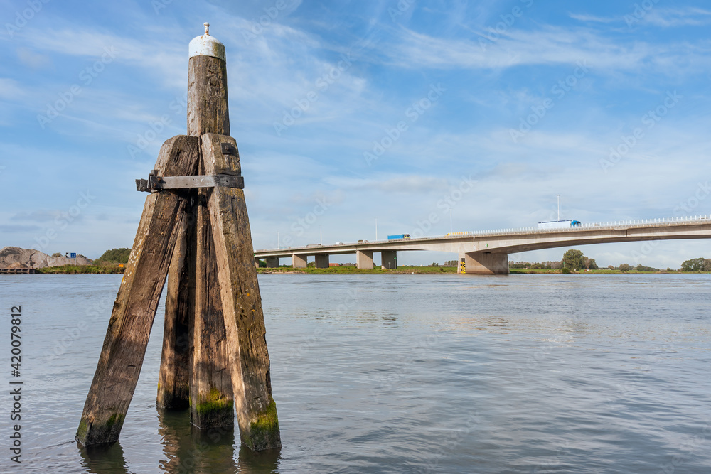 Dutch river IJssel with wooden bollard and concrete road bridge