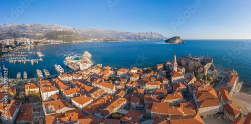 Aerial View of Budva Old Town and sandy beach in a beautiful spring day. Top view from drone on the old fortress and azure sea. Horizontal panorama, Montenegro