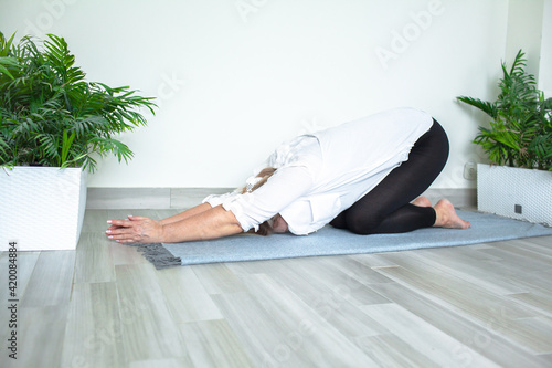 Middle-aged woman doing yoga at home for stretching and being healthy