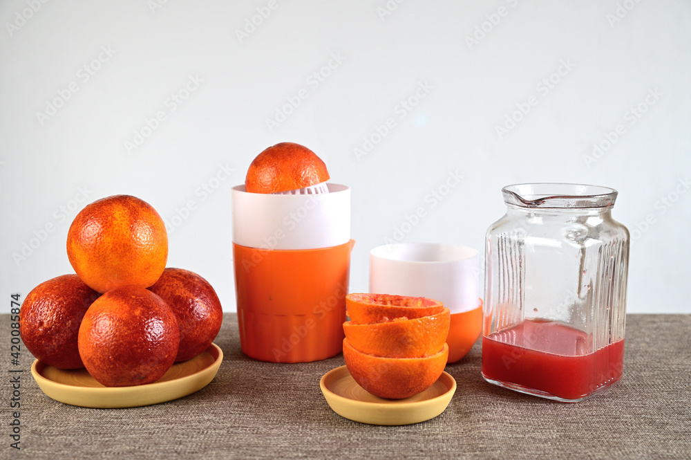 Manual juicer. There are several oranges nearby. There is a decanter with squeezed juice.