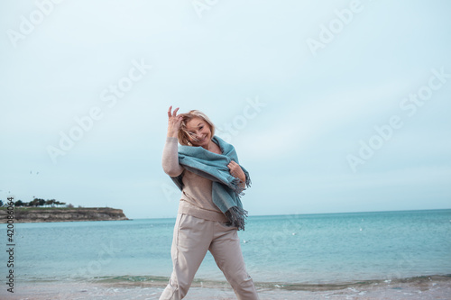 Beautiful middle-aged woman in blue warm scarf walking in the beach of the sea © Вероника Зеленина