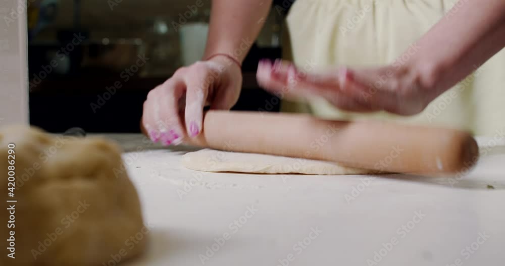 A woman spreads the raw dough on the kitchen table at home. A woman spreads the raw dough on the kitchen table at home.