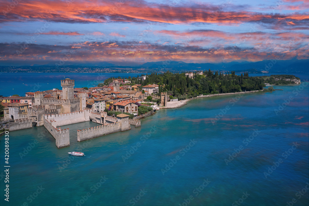 Sirmione, Lake Garda, Italy. Reflections of the castle in the water in the background pink sky at sunset. Italian castle on the water. The famous Sirmione Castle. Frontal close aerial view.