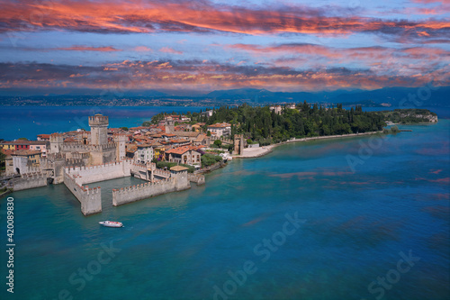 Sirmione, Lake Garda, Italy. Reflections of the castle in the water in the background pink sky at sunset. Italian castle on the water. The famous Sirmione Castle. Frontal close aerial view.