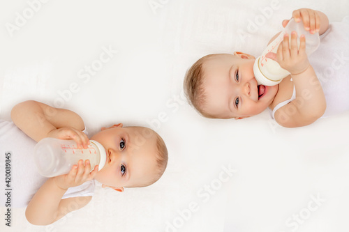 twin babies boy and girl with a bottle of milk on a white bed at home, baby food concept, place for text photo