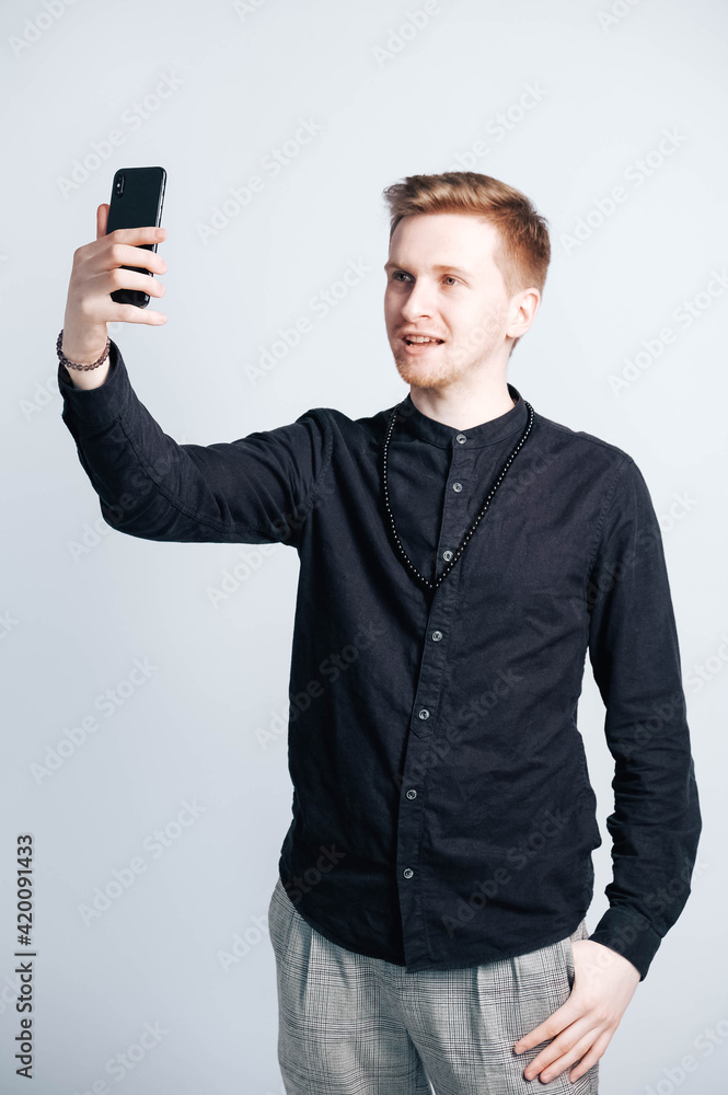Portrait young man in a black shirt with a smartphone in his hands on a white background. Copy, empty space for text Portrait young man in a black shirt with a smartphone in his hands on a white background. Copy, empty space for text