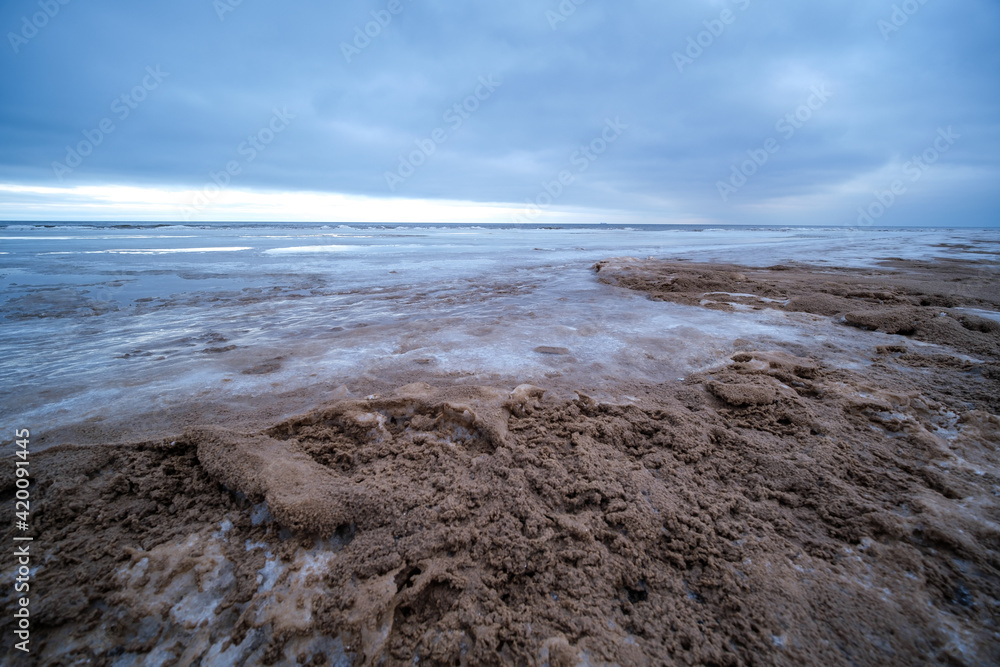 icy winter beach near the sea with frozen sand and ice blocks in the water