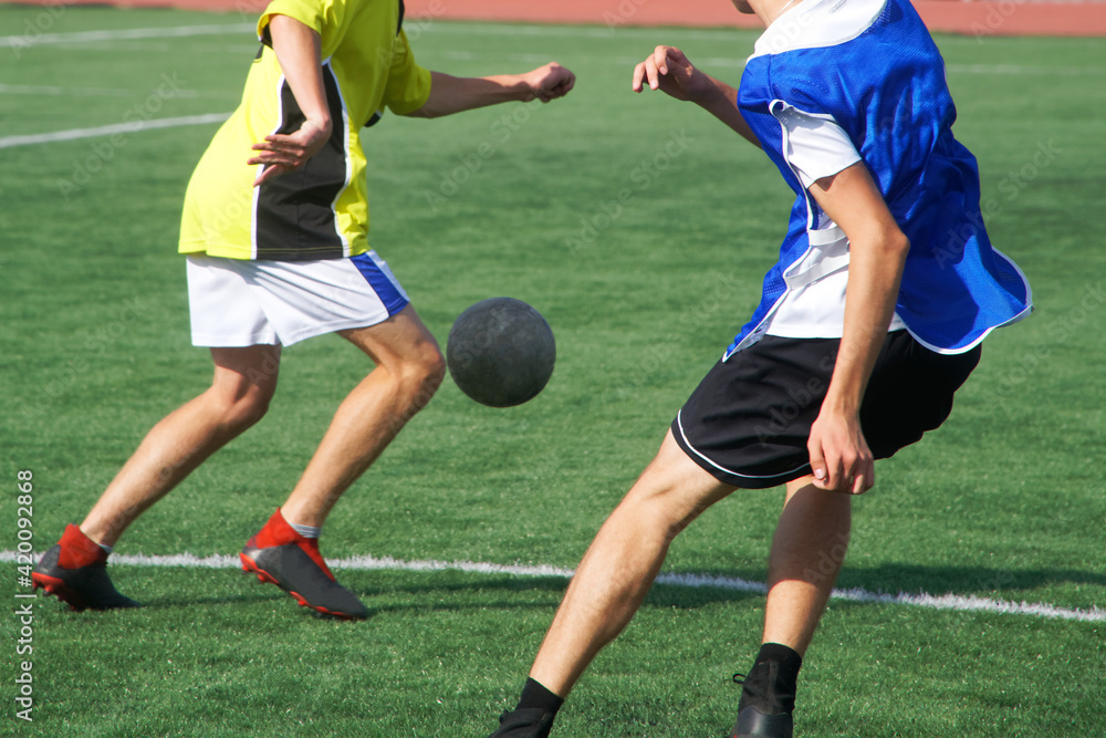 Two young men practice soccer dribbling on a green artificial field. Without a face