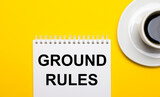 On a bright yellow background, a white cup with coffee and a white notepad with the words GROUND RULES