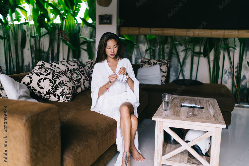 Slender female taking medicine while sitting on couch at home Slender female taking medicine while sitting on couch at home
