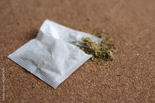 Chamomile teabag on cork board. Torn teabag with chamomile tea leaves spilling out