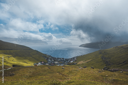 Sun shining on small village on the the northern most village on Stremoy in the Faroe Islands with blue sky and flowers.