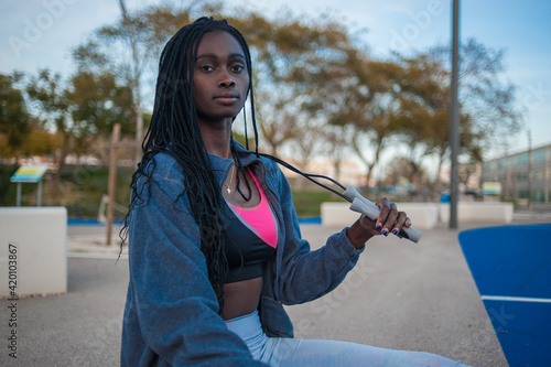 front view of a black woman sitting on a bench holding a rope ready to exercise. Fitness routine