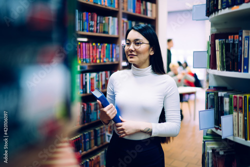 Ethnic young student standing with blue book in college library