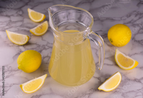 A jug of lemon juice on a white marble background. Top view.