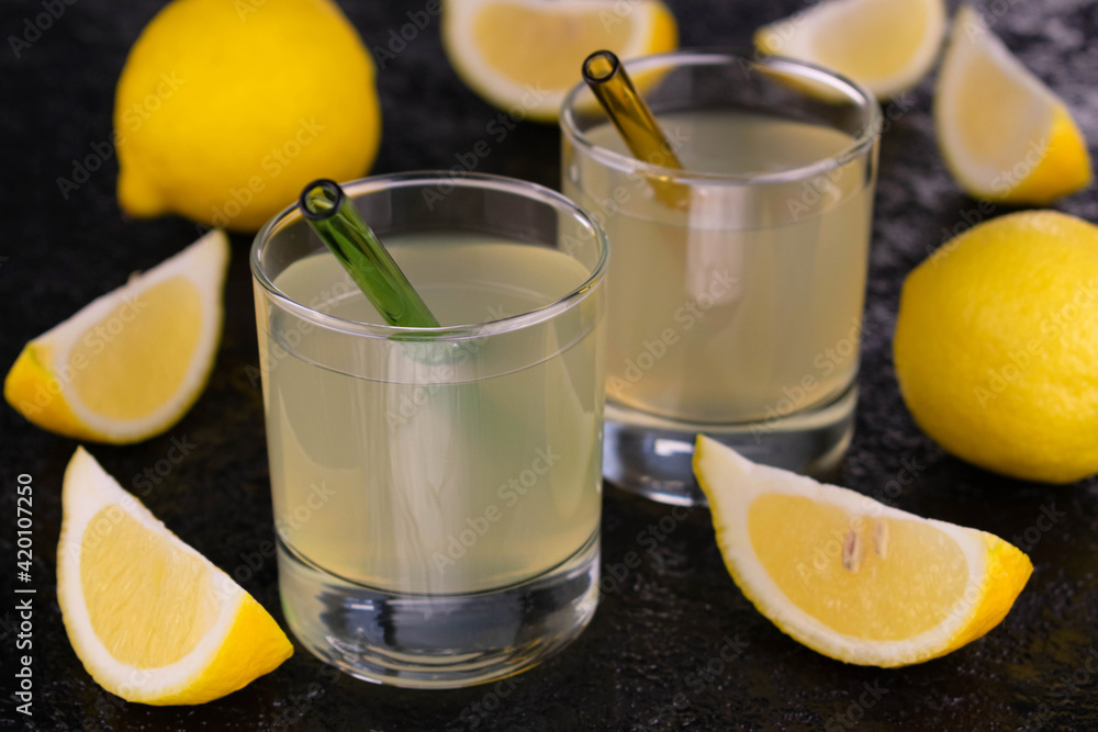 Two glasses with lemon juice on a black background.
Two glasses with lemon juice on a black background.