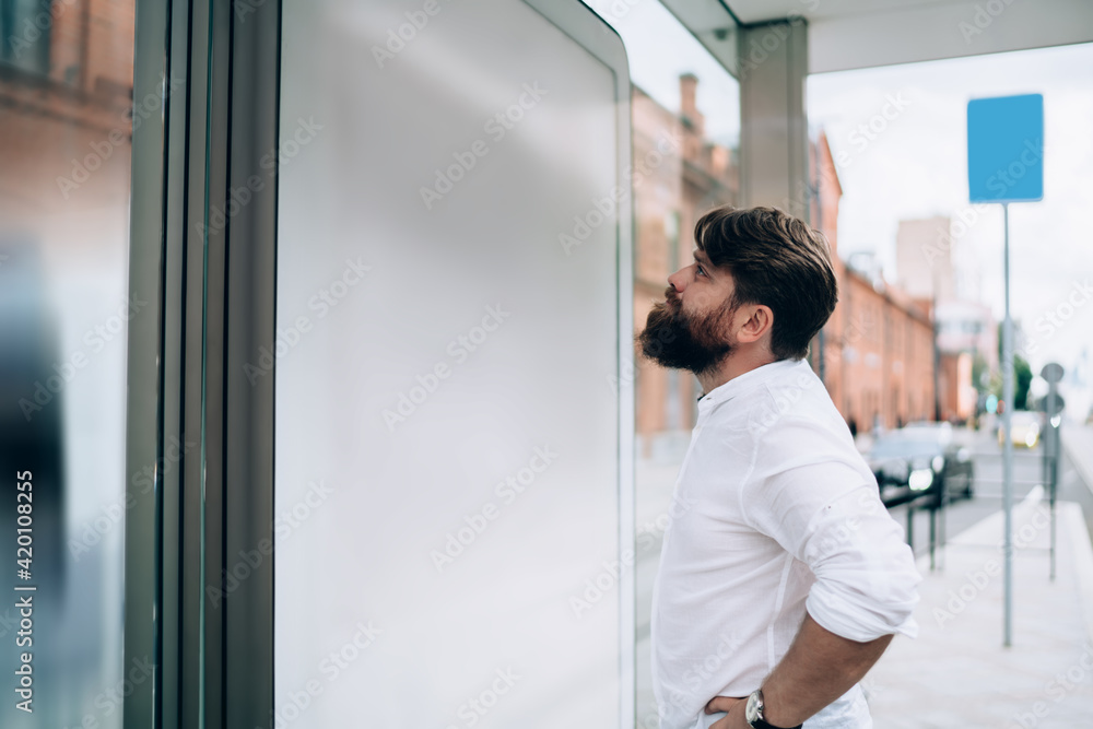 Thoughtful bearded businessman looking at screen on bus stop