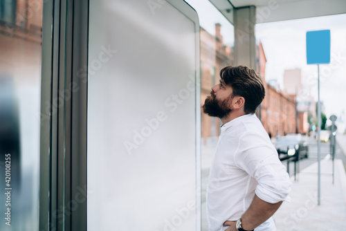 Thoughtful bearded businessman looking at screen on bus stop