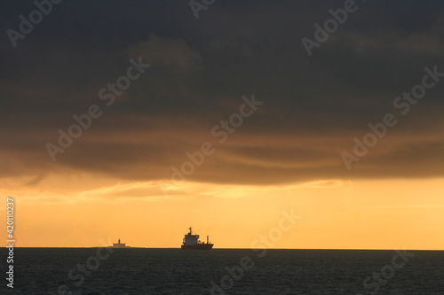 cargo sur la mer avec un phare au loin et le coucher de soleil près du port de Lisbonne au Portugal