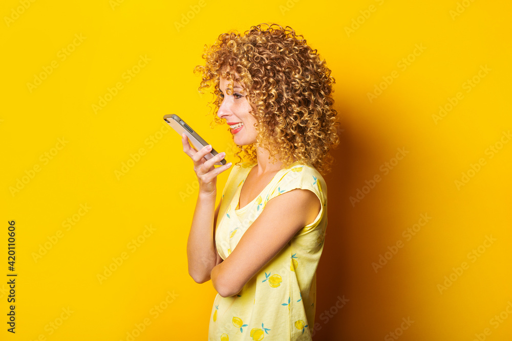 curly young woman writes a voice message on the phone on a yellow background. curly young woman writes a voice message on the phone on a yellow background.