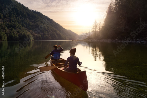 Couple friends canoeing on a wooden canoe during a colorful sunny sunset. Cloudy Sky Artistic Render. Taken in Harrison River, East of Vancouver, British Columbia, Canada.