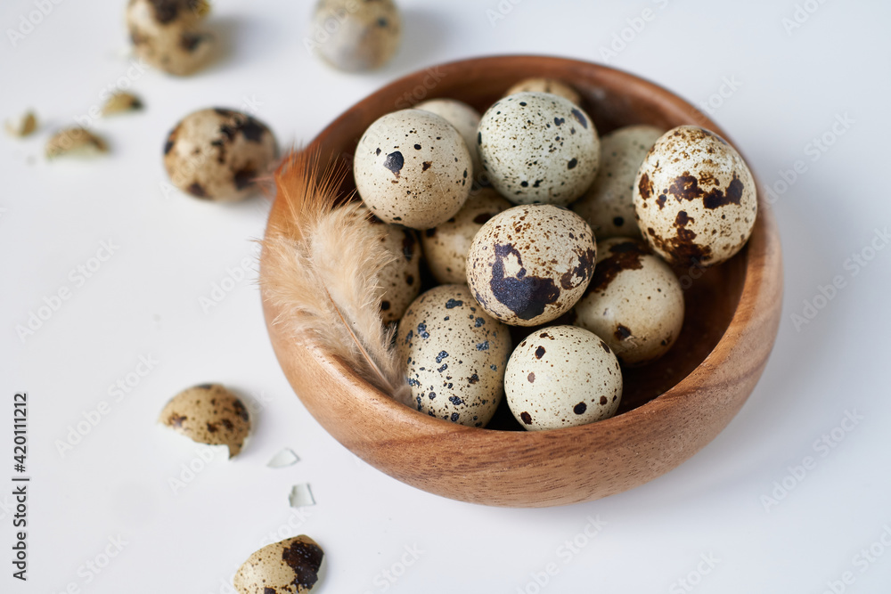 Obraz premium quail eggs in a wooden bowl painted with a feather on a white table. Easter concept Copy space