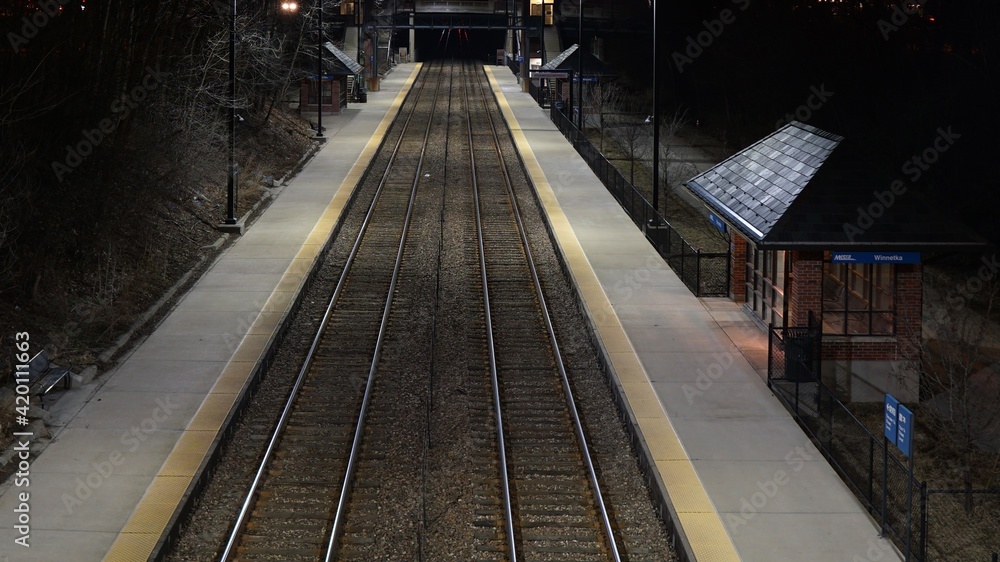Empty Metra Union Pacific North commuter rail train tracks at night at suburban station.
