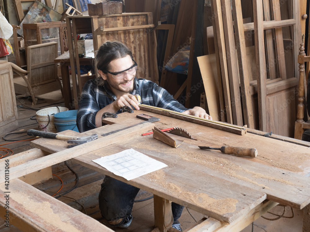 Handsome Caucasian carpenter using a tape measure for measuring woodwork in the carpentry workshop. Manufacture of wood products... Handsome Caucasian carpenter using a tape measure for measuring woodwork in the carpentry workshop. Manufacture of wood products...
