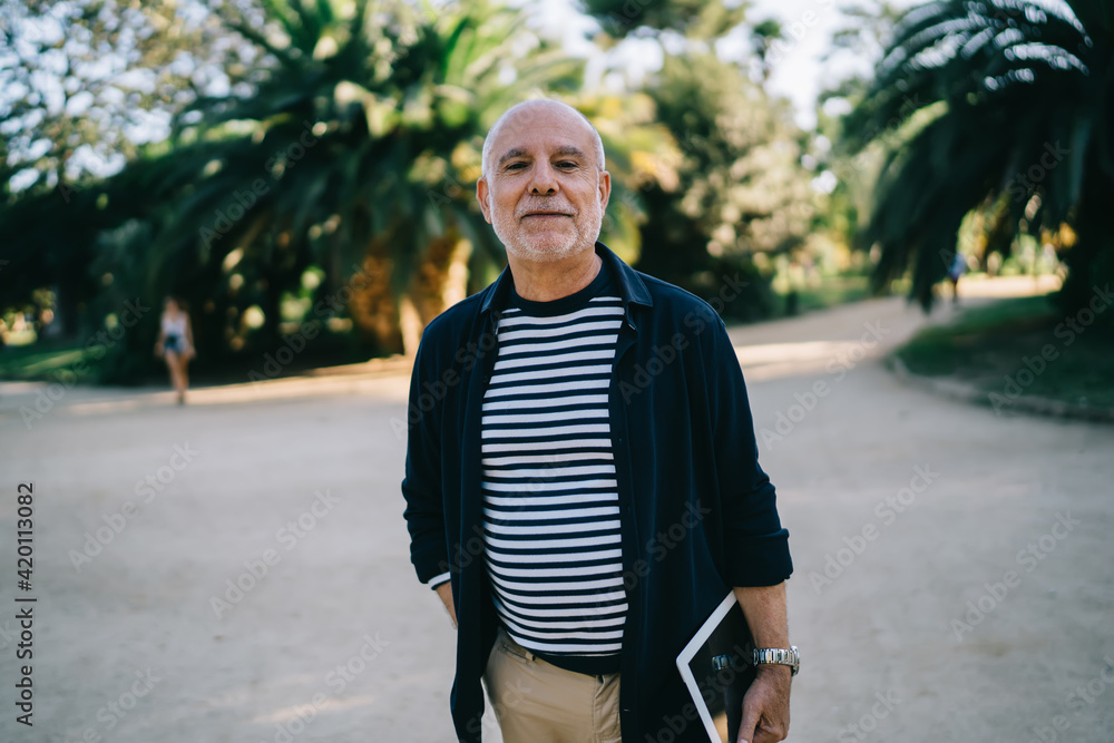 Obraz premium Half length portrait of aged senior traveller with modern touch pad gadget looking at camera during free time in city, casual dressed male tourist 60s with digital tablet posing on retirement