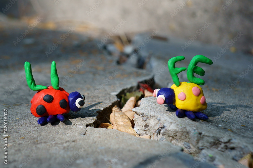 Obraz premium Figurines of two ladybirds made of plasticine. The figures are placed opposite each other. There's a crack between them. Next to it is the inscription life.