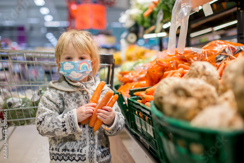 Cute toddler child, boy, wearing medical mask in supermarket store photo